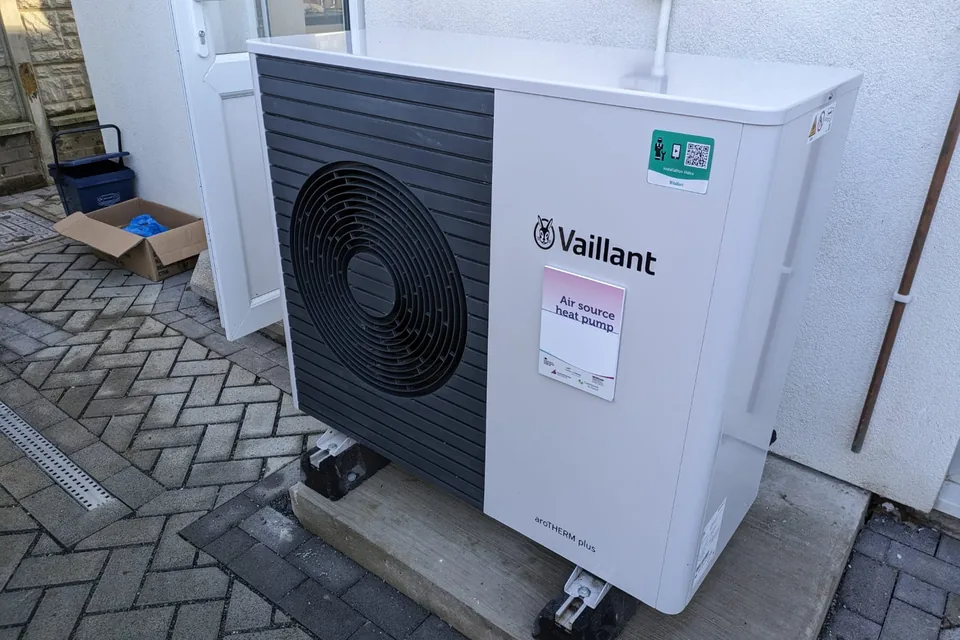 Unité extérieure de pompe à chaleur air-eau, posée sur des dalles contre le mur d'une maison